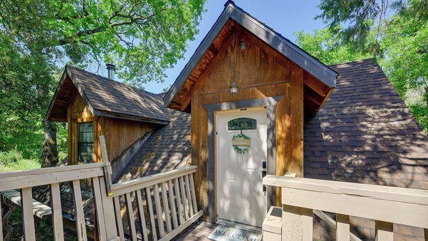 A wooden cabin with a white door and a welcome mat, surrounded by a wooden deck and trees. - 'Lakeside Bear Lodge' Studio: 9 Mi to Bass Lake! (Wishon)