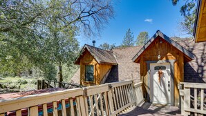 A wooden cabin with a deck, a chimney, and a door with a hanging ornament. - 'Lakeside Bear Lodge' Studio: 9 Mi to Bass Lake! (Wishon)