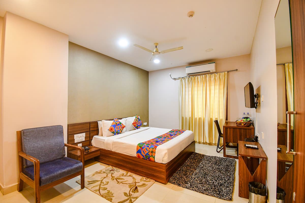 A hotel room with a bed, a chair, a desk, a mirror, and a ceiling fan.