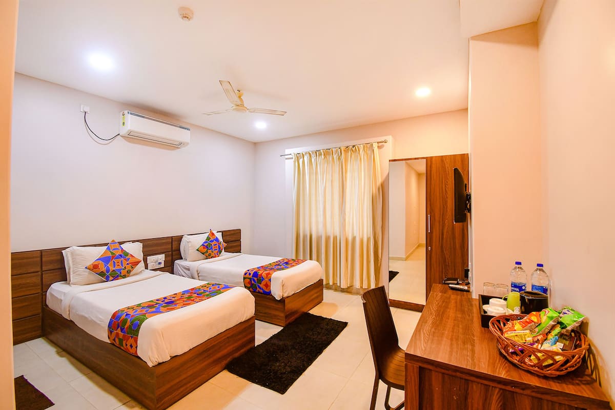 A hotel room with two beds, a desk, a chair, a dining table, a ceiling fan, and an air conditioning unit.
