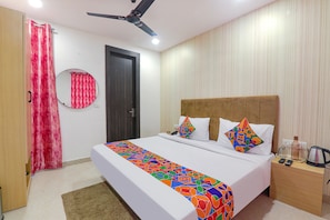 A hotel room with a bed, a nightstand, a mirror, a ceiling fan, and a door. - Fabhotel The Comfort (Prayagraj)