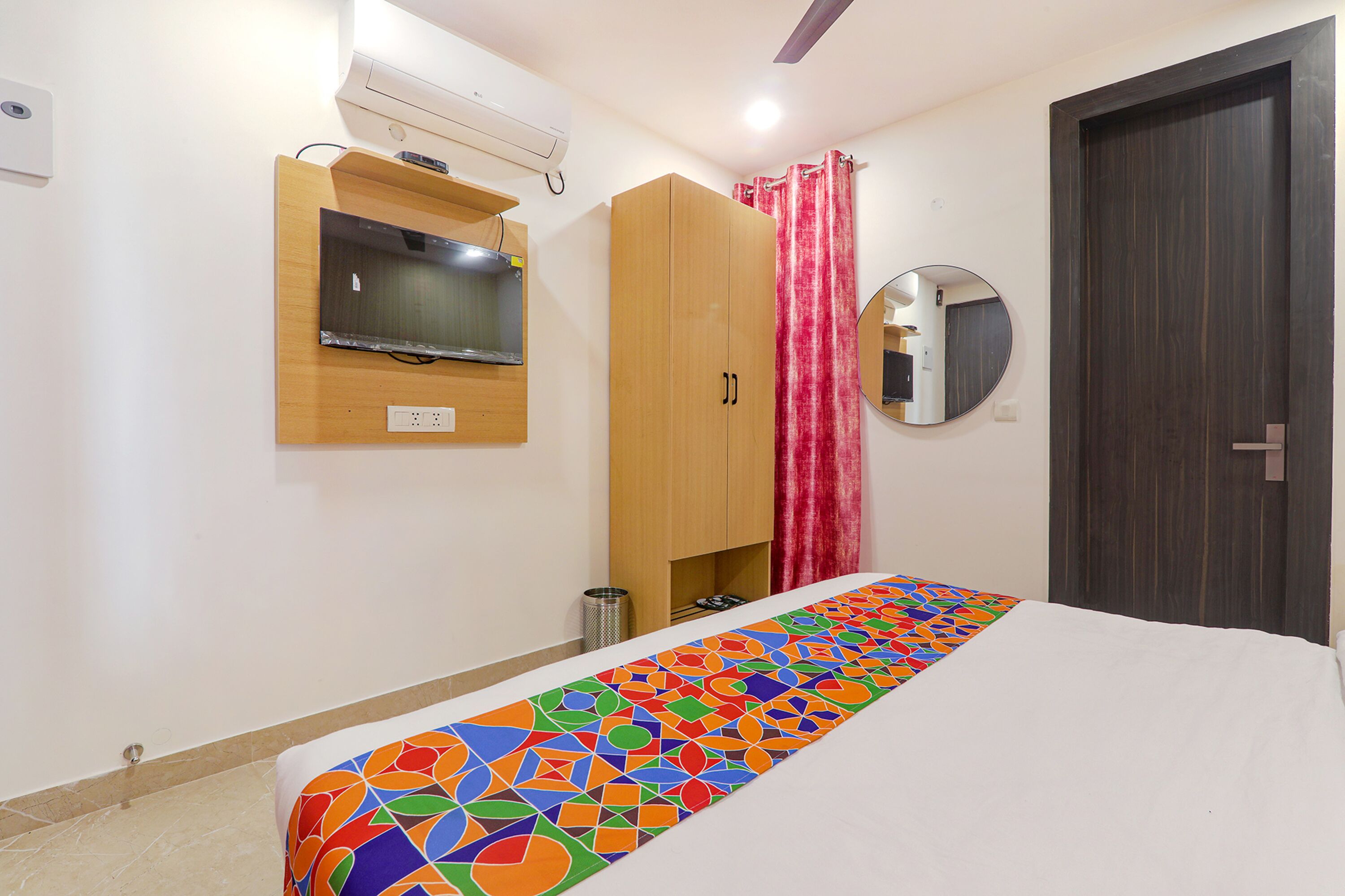Un dormitorio con cama, armario, televisor montado en la pared, espejo y cortina.