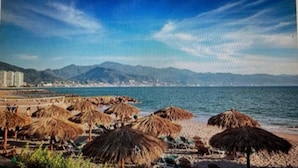 A beach with thatched umbrellas and a view of mountains in the background. - Vidanta Mayan Condo (Puerto Vallarta)