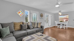 A modern living room with a grey sofa, patterned ottoman, and a dining area with a white table and chairs. - Unique A-Frame Heated pool & Firepit  (Cocoa)