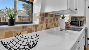 A modern kitchen with white cabinets, a white countertop, a microwave, and a potted plant on the windowsill. - Unique A-Frame Heated pool & Firepit  (Cocoa)
