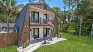 A two-story house with a balcony, a flag, and a pool in the background. - Unique A-Frame Heated pool & Firepit  (Cocoa)