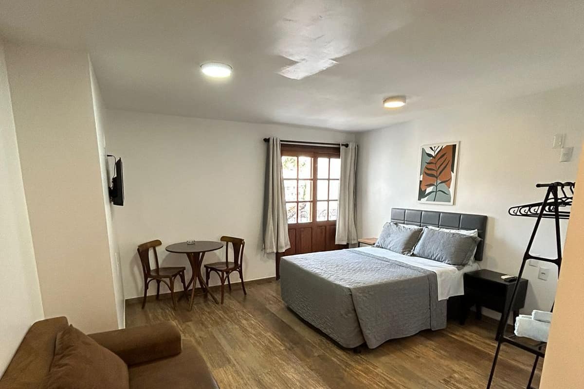 Habitación de hotel con una cama grande, un sofá, una mesa de comedor y una ventana con cortinas.