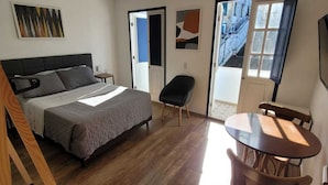 Un dormitorio moderno con cama, escritorio y silla. Se ve una ventana con vista a edificios.