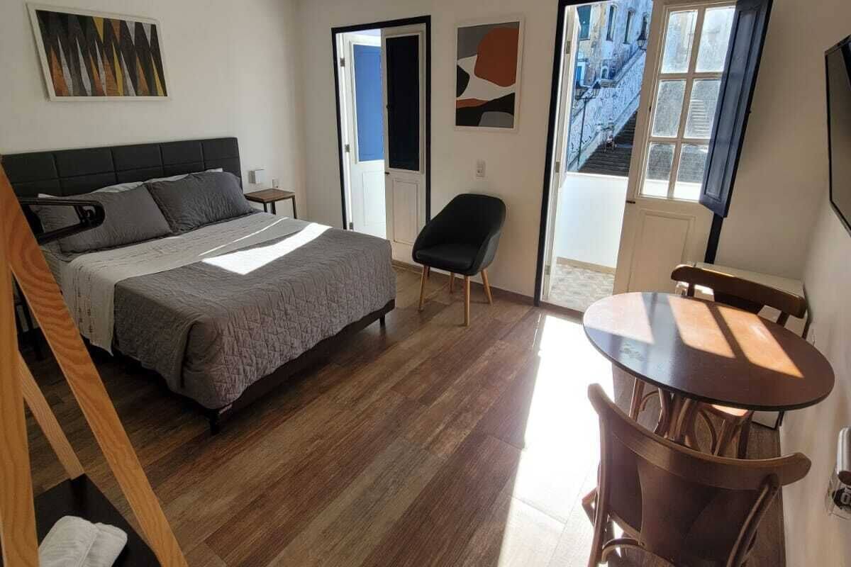 Un dormitorio moderno con cama, escritorio y silla. Se ve una ventana con vista a edificios.