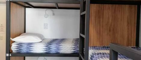 Ein Schlafzimmer mit Etagenbetten, drei Ebenen, jede mit einem gemusterten Bett und Kissen.