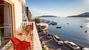 A balcony with a table, red chairs, and a view of the sea with boats. - ACIKA apartments Rafailovici (Becici)