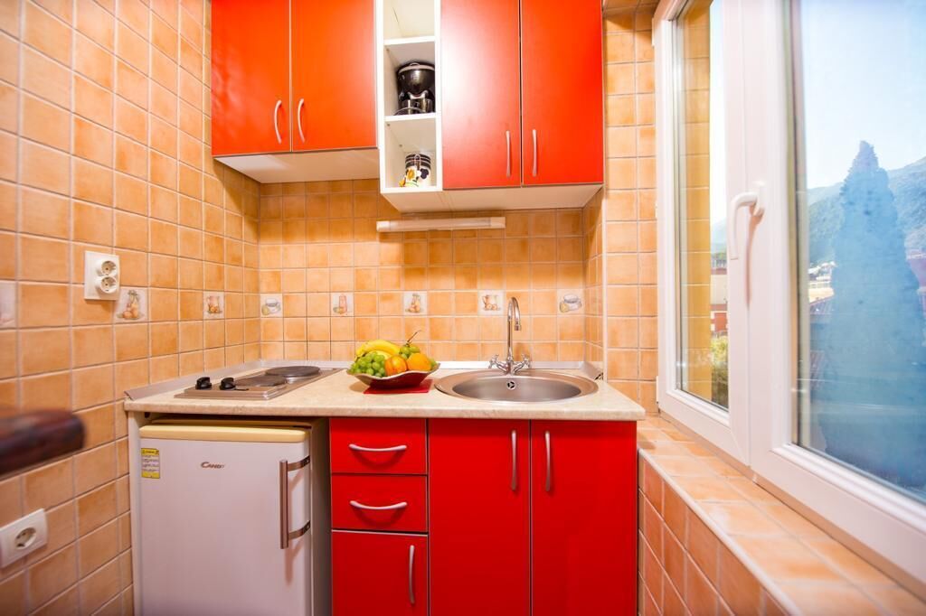 A kitchen with red cabinets, a white refrigerator, and a window with a view of a mountain.