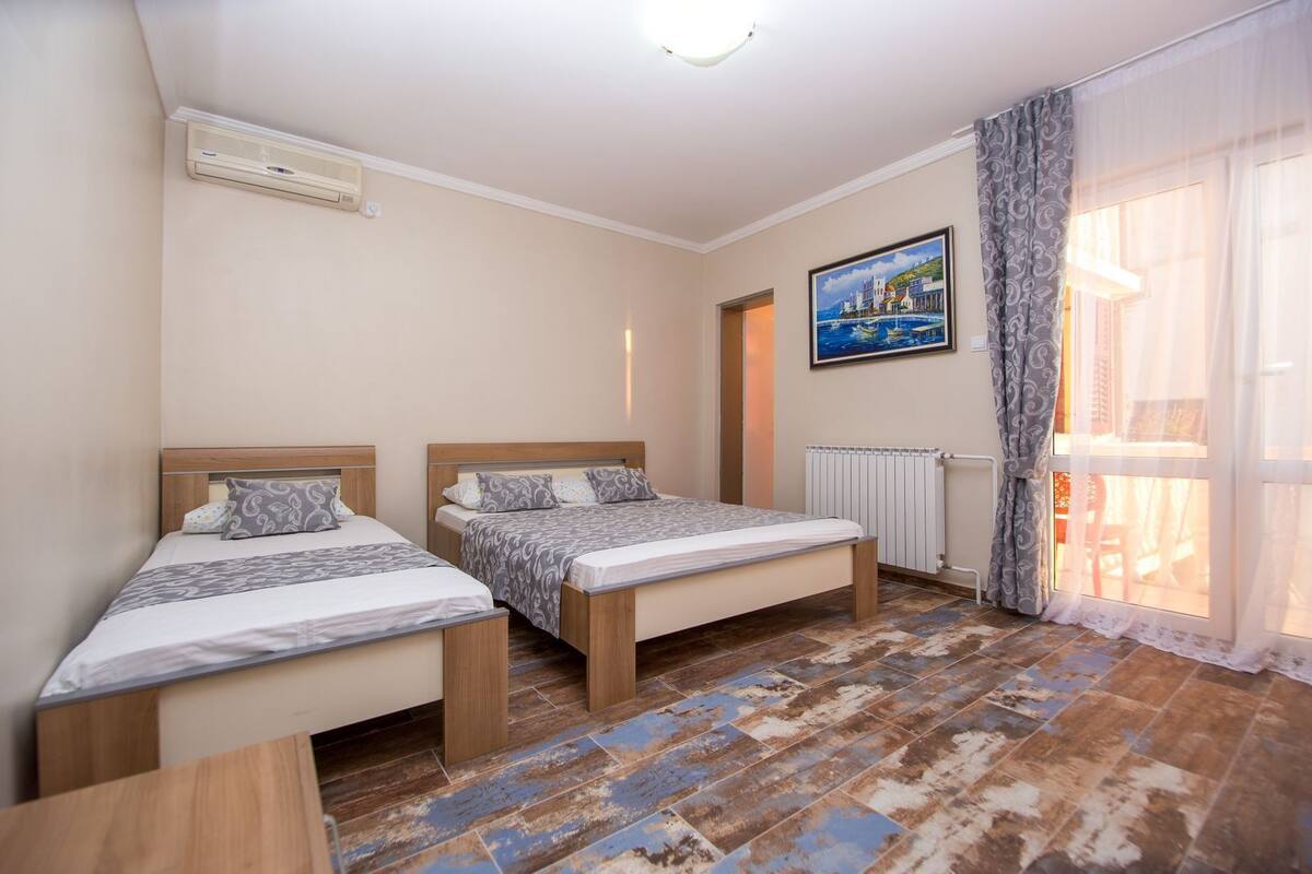 Quarto de hotel com duas camas de solteiro, um radiador, um quadro e uma janela com cortinas.