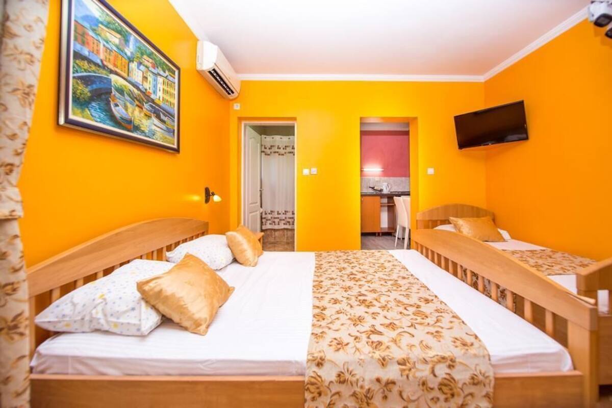Quarto de hotel com duas camas de madeira, uma televisão na parede e uma pintura representando uma cena de canal.