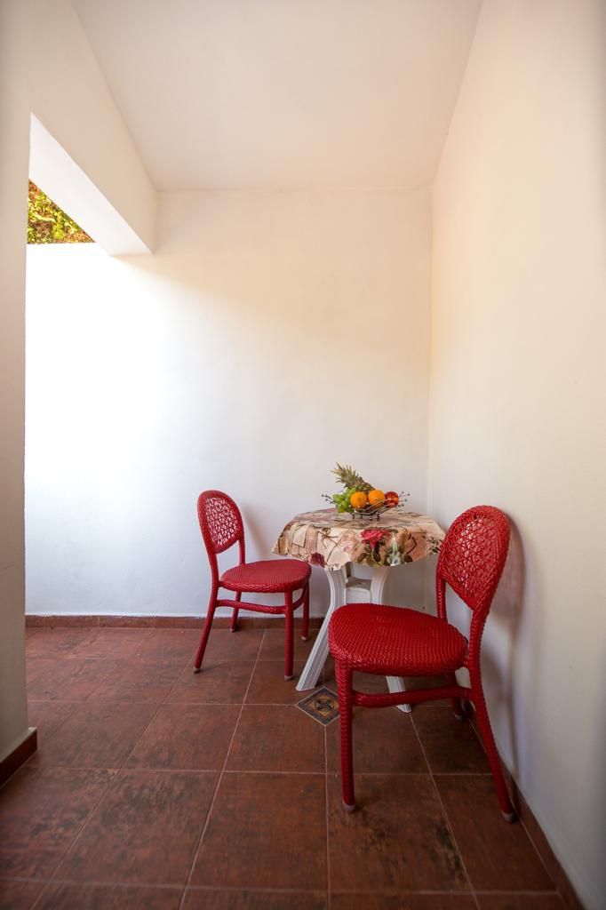 Una habitación pequeña con dos sillas rojas, una mesa con mantel floral y un frutero.