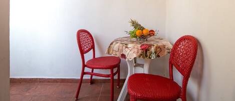Una habitación pequeña con dos sillas rojas, una mesa con mantel floral y un frutero.