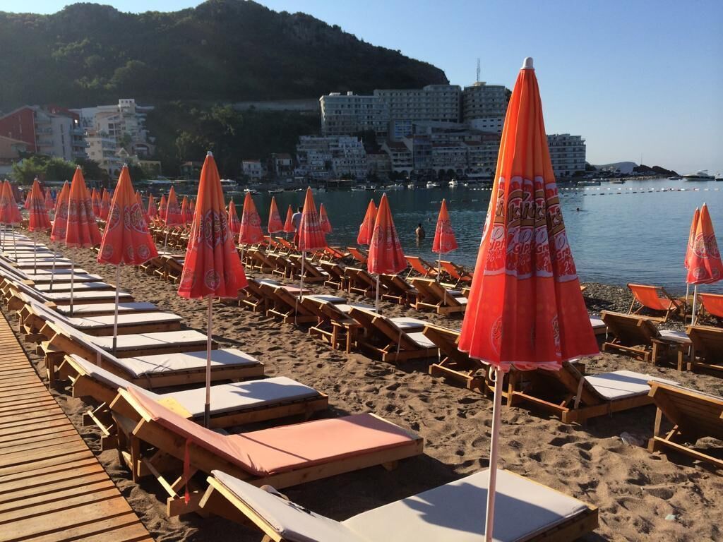 A beach with rows of sun loungers and orange umbrellas.