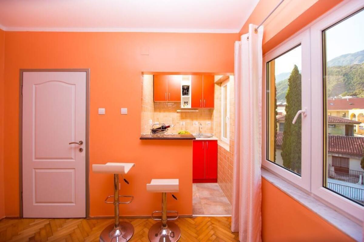 Cozinha compacta com porta branca, dois bancos altos e janela com vista para uma paisagem montanhosa.