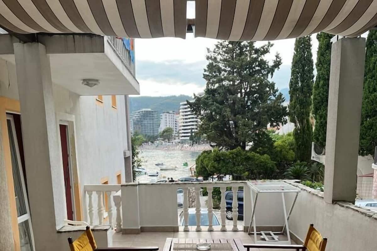 Uma varanda com mesa e cadeiras, com vista para um corpo de água e edifícios.