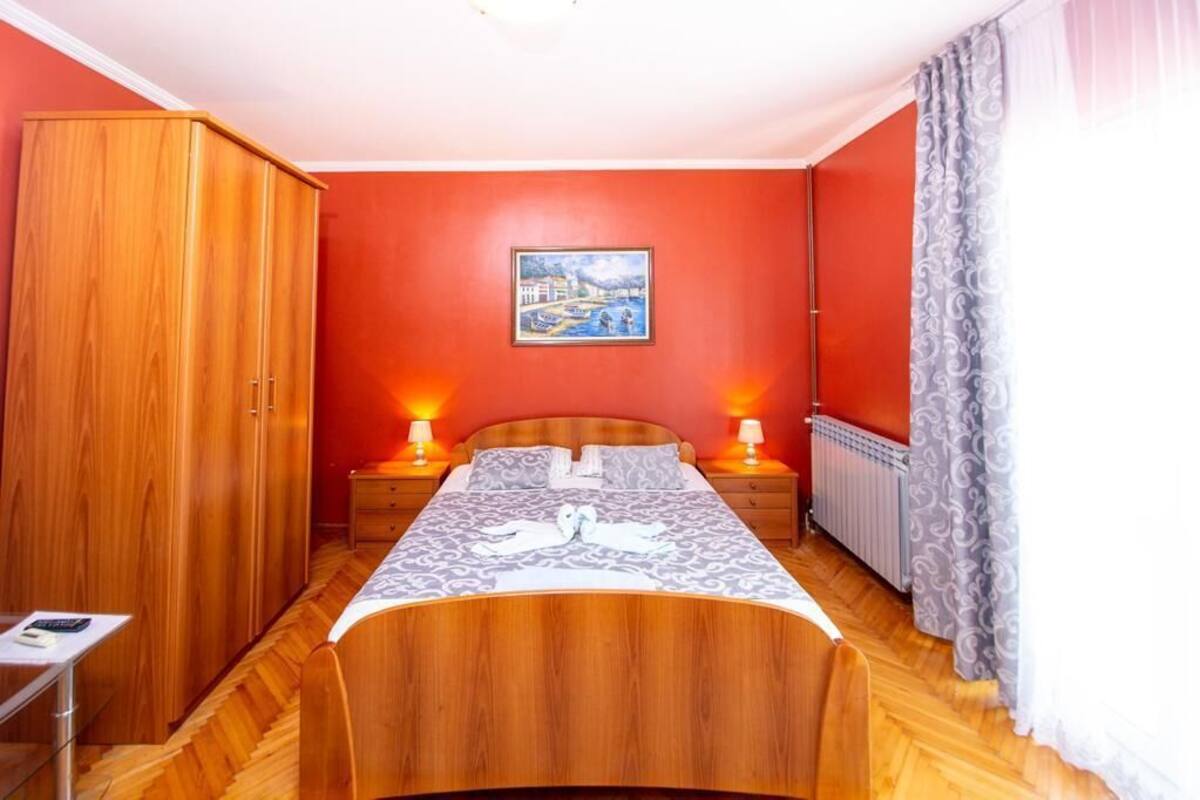 Quarto com cama de madeira, duas mesinhas de cabeceira, um guarda-roupa e um quadro na parede.