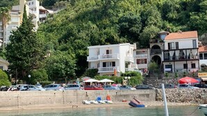 A coastal area with a marina, parked cars, and buildings with balconies overlooking the water. - ACIKA apartments Rafailovici (Becici)