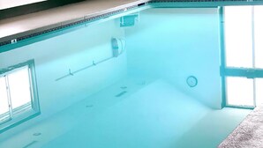 Une piscine intérieure à l’eau claire, dotée d’un plongeoir et d’une fenêtre sur l’un des côtés.