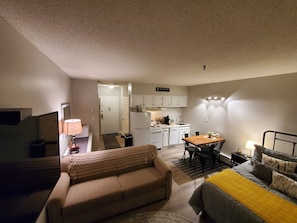A compact living space with a kitchenette, a sofa, a dining table, and a bed.