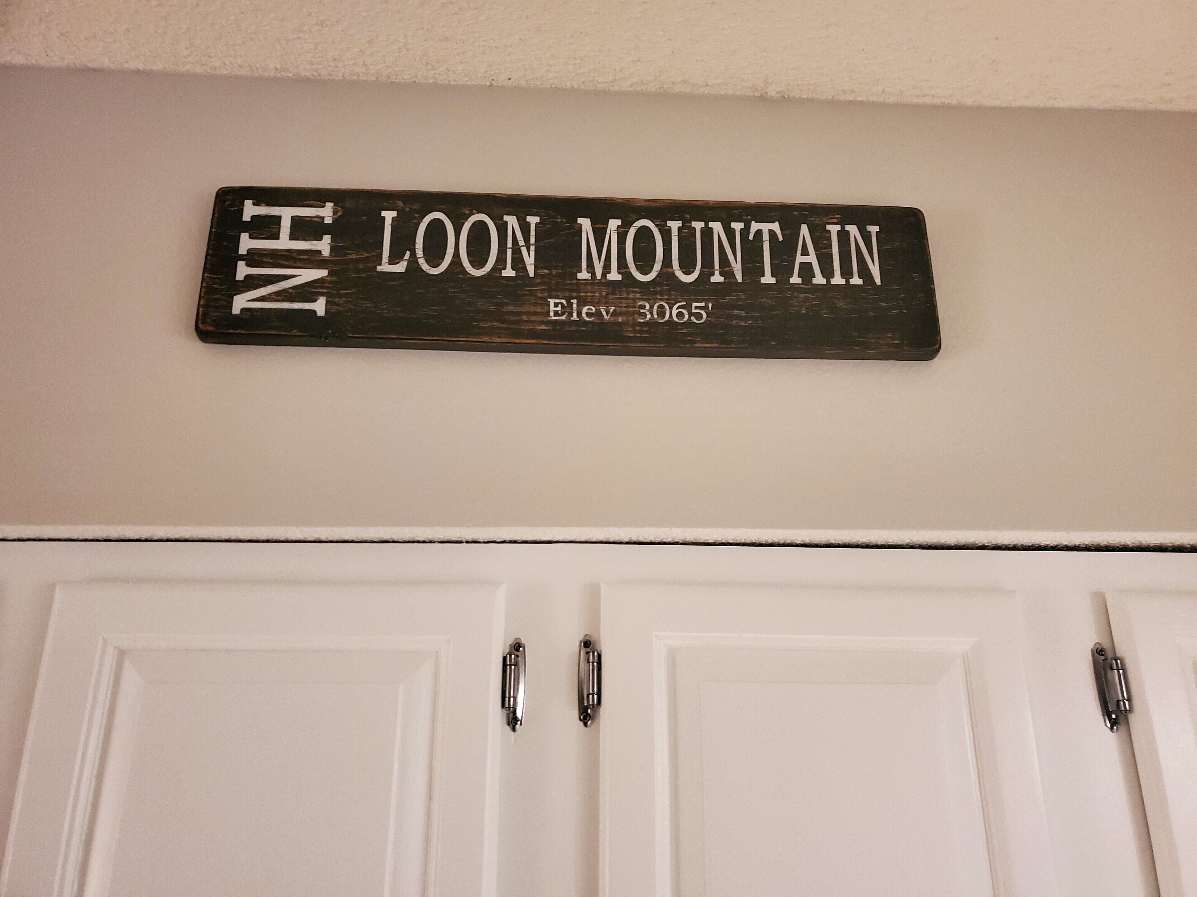 A wooden sign with "NH Loon Mountain" and "Elev. 3065" indicating the location.