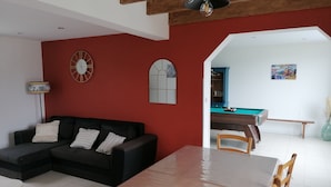Una sala de estar con un sofá modular negro, una mesa de comedor de madera y una mesa de billar.
