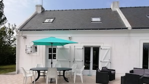 Una casa blanca con un patio que tiene una mesa, sillas, un paraguas verde y asientos exteriores.