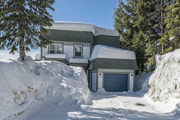 Una casa de dos pisos con garaje, rodeada de nieve y árboles.