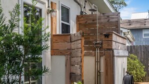 Una pérgola de madera con rociador incorporado, una pared exterior blanca y una ventana.