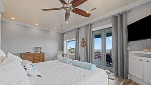 A bedroom with a large bed, a ceiling fan, a dresser, a TV, and a view of the outside. - Luxury Gulf-View Beach Retreat Pool, Deck, Steps to Sand, Pet-Friendly, Sleeps 9 (Gulf Breeze)