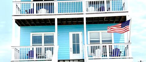 A multi-story building with a blue exterior, white railings, and an American flag.