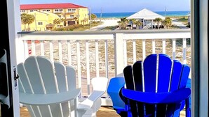 A deck with white and blue Adirondack chairs overlooking a beach with buildings in the background. - Luxury Gulf-View Beach Retreat Pool, Deck, Steps to Sand, Pet-Friendly, Sleeps 9 (Gulf Breeze)