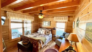 A cozy log cabin bedroom with a bed, a chair, a table, and a window with a view.