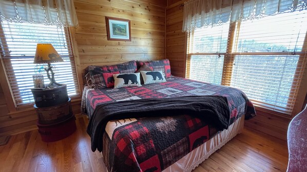 A cozy wooden cabin bedroom with a bed, a nightstand, and a window with blinds.