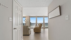 En hall som leder ut till en balkong med utsikt, en randig soffa och en beige fåtölj.