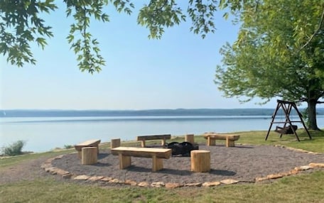 A circular seating area with benches and a swing set, surrounded by a grassy field with a view of a calm body of water.