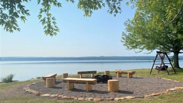 A circular seating area with benches and a swing set, surrounded by a grassy field with a view of a calm body of water.
