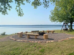 A circular seating area with benches and a swing set, surrounded by a grassy field with a view of a calm body of water. - Baraga Lakeside Inn (Baraga)