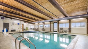 An indoor swimming pool with a wooden ceiling, clear pool water, and a few lounge chairs.