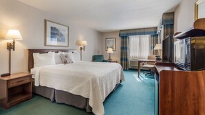A hotel room with a large bed, a desk with a chair, a television, and a minibar.