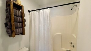 A bathroom with a shower, toilet, and a shelf with towels. - The Klassic Inn (Higden)