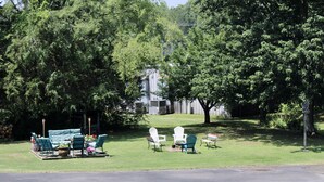 A grassy outdoor area with a patio set and Adirondack chairs, surrounded by trees. - The Klassic Inn (Higden)
