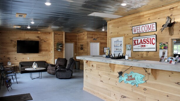 A wooden interior with a reception desk, a flat-screen TV, and a sign reading "Welcome Classic Inn." - The Klassic Inn (Higden)
