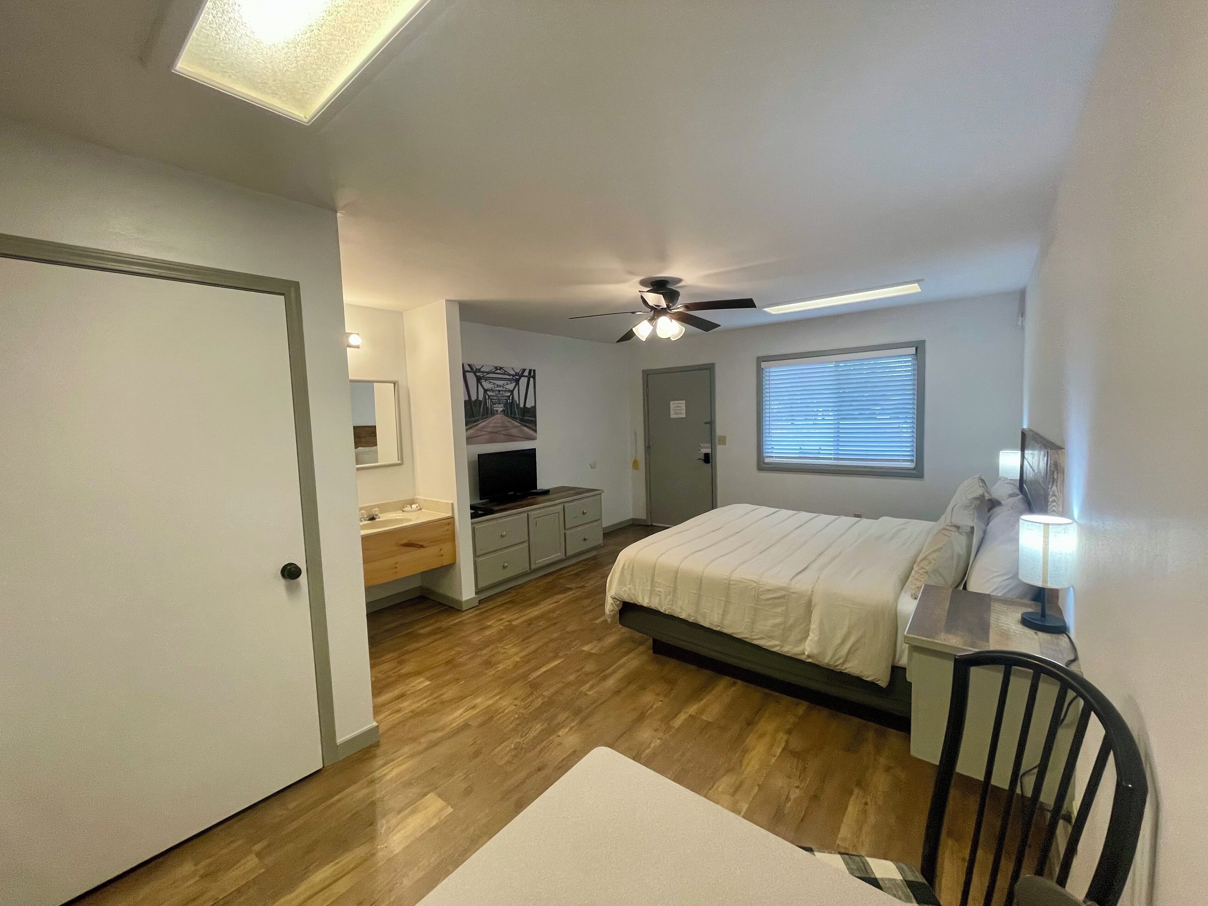 Ein Schlafzimmer mit Bett, Schreibtisch, Stuhl, Fernseher und Fenster.