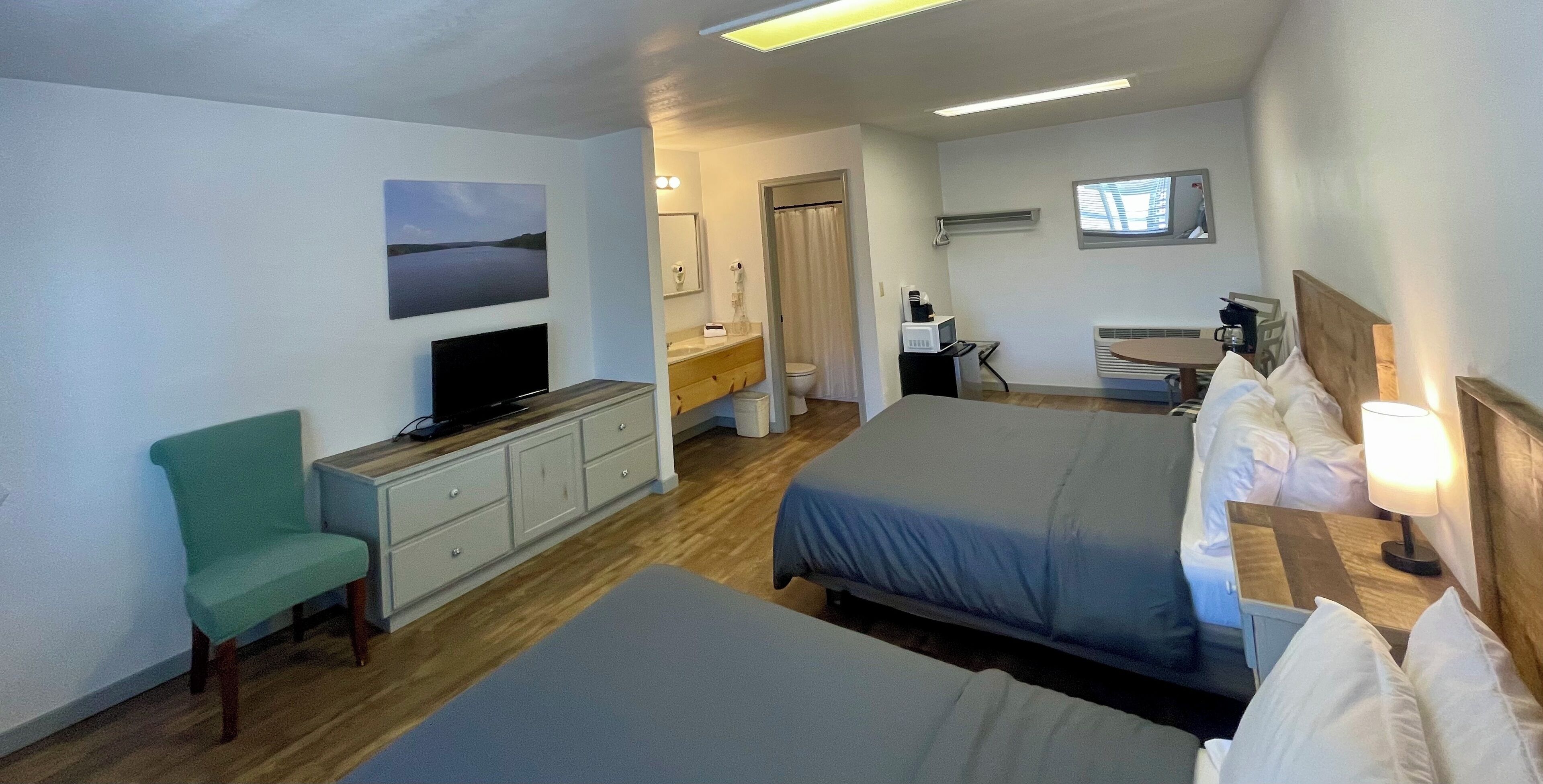 Ein Hotelzimmer mit zwei Betten, einem Fernseher, einem Schreibtisch mit einem Computer, einem Stuhl und einem im Hintergrund sichtbaren Badezimmer.