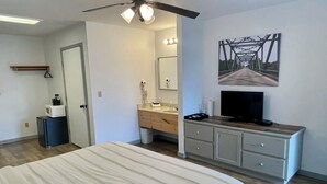 A hotel room with a bed, a TV, a vanity, and a painting on the wall. - The Klassic Inn (Higden)