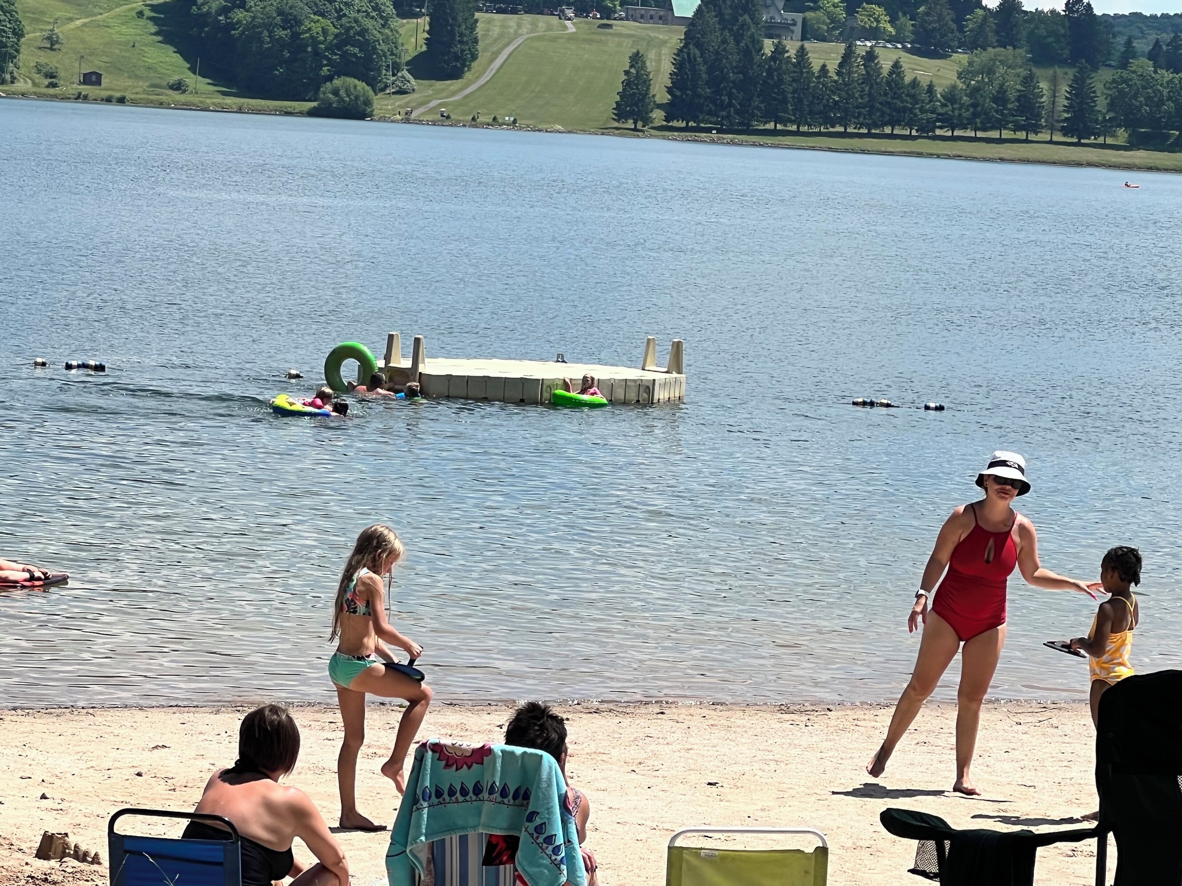 A lakeside scene with people in swimwear, a dock, and a grassy area.